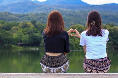 Genç bir LGBTQ çifti, LGBTQ insanlarının sevgisini anlamak ve kabul etmek amacıyla bir kalp sembolünü birlikte göstermek için ellerini kullanıyor.