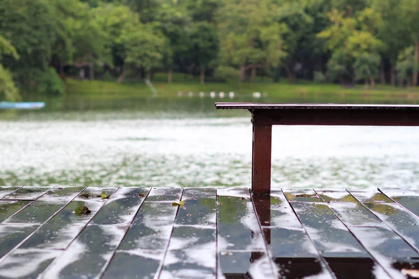 Long wooden benches and wooden decking that had been soaked in rain after the rain storm had passed leaving rain on the ground and on the benches making the area seem empty and uninhabited.