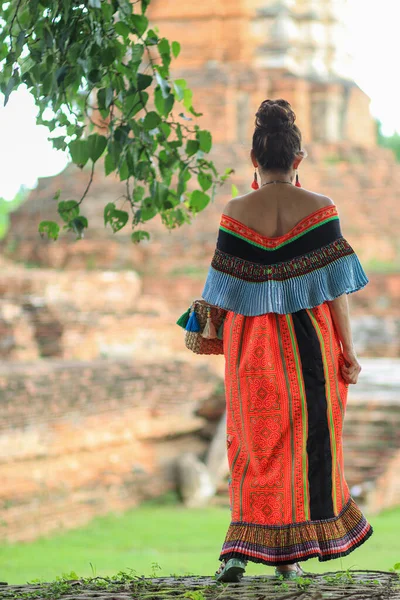 An elderly woman in traditional woven clothes is walking to see the scenery of an ancient city in Thailand and wants to dress in traditional woven clothes to match the atmosphere of the ancient city.