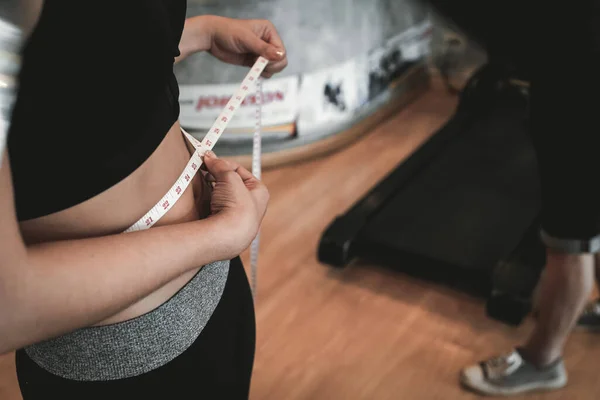 A beautiful woman with a waist tape measure and she is using her hands to hold the tape around her waist after taking a fat breakdown course to lose weight for a period to check the results.