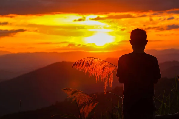 Silhouette of an old man watching beautiful lights during Twilight and watching sunset on mountains alone in loneliness. An old man is traveling and watching view of the setting sun on high mountains.