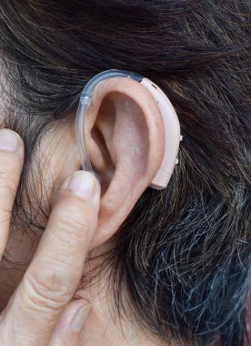 Asyalı yaşlı kadının kulağında işitme cihazı var. Sağırlık sorunu var..