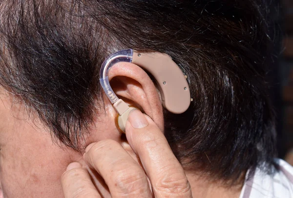 Electronic hearing aid device in the ear of Asian old man with total deafness.