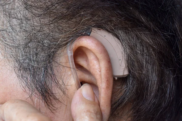 Electronic hearing aid device in the ear of Asian old man with total deafness.