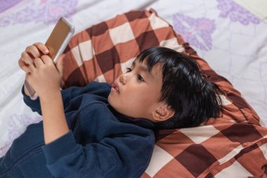 Asyalı çocuklar sırt üstü yatıp kablosuz teknolojiye bağlı akıllı telefona bakıyorlar. Evde kal.