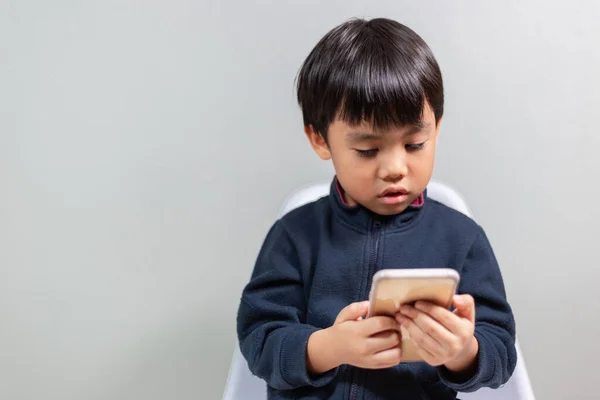 Chłopiec Siedzi Białym Krześle Pokoju Szare Tło Korzystanie Smartfona Nauki — Zdjęcie stockowe
