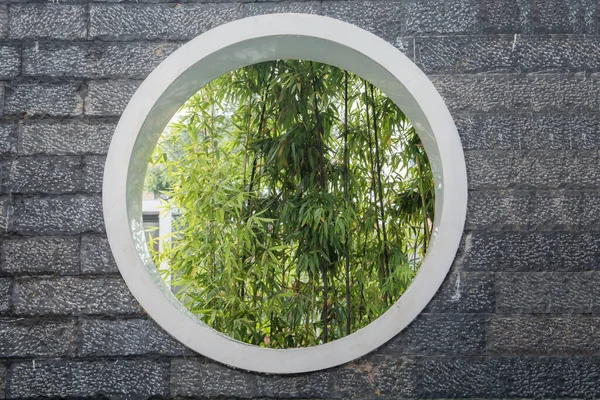 Bamboo leaves through a big  circle window, in a stones pavement wall Pudong district, Shanghai, China.
