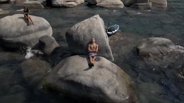 Młoda para relaksująca się na skałach jeziora — Wideo stockowe