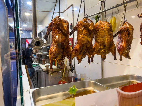 ATHENS, GREECE - JANUARY 15, 2022: Close up of delicious crispy roasted Peking duck hanging in a Chinese restaurant kitchen window. Several cooked goose displayed. Food background with copy space.