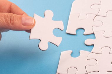 Mavi yüzeyde bulmaca parçalarını tutan eller. Beyaz yapboz oyun dokusu. Uyumlu, son kayıp parça yerleştiriliyor. İş ve takım çalışması problem çözme geçmişi. Metin eklemek için boşluk kopyala, kapat.