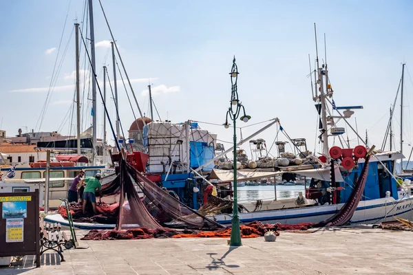 Yunanistan 'ın Aegina adası - 04.27.2022: Yunan balıkçılar Aegina Adası limanında balık ağlarını çekiyor ve astarlıyorlar. İş ve iş aletleri. Güneşli bir günde yerel endüstriyel iş geçmişi