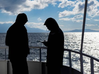 Güneşli kış gününde gemi güvertesinde cep telefonu uygulamasına bakan iki kişi. Seyahat başvurusu, internet otel rezervasyonu, seyahat tavsiyesi için mobil kayıt. Gezgin yolda. Çevrimdışı kablosuz harita kullanılıyor