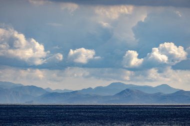 Dağ, okyanus plajı ve bulutlu gökyüzü arka planı mavi tonlarda. Dağları ve fiyortları olan tropik deniz manzarası. Tatil tatili macera konsepti. 
