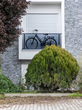 Dağ bisikleti, penceresi kapalı bir apartmanın balkonunda depolanmış. Bahçedeki yeşil çalı. Rahatlama zamanı. Covid-19 tecrit. Spor geçmişi