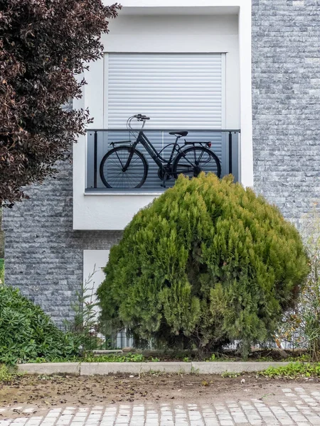 Mountain bike stored at balcony of a residential apartment with closed window shutter. Green bush in the garden. Time for relaxing. Covid-19 lock-down. Sports background
