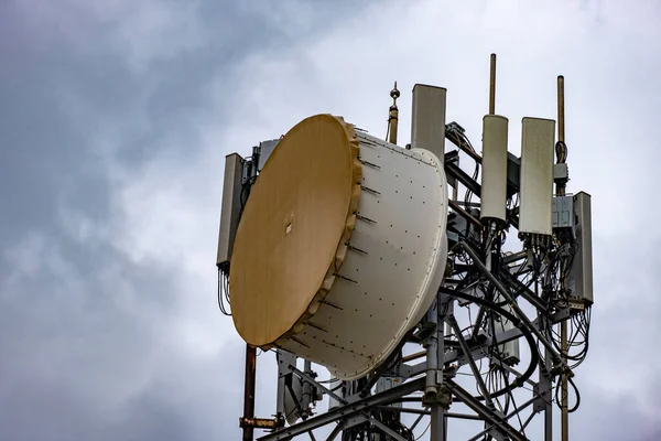 Bass drum style microwave antennas on tall tower, closeup. 5G Cellular communication for mobile phone and video data transmission. Telecommunication connection point against grey cloudy sky