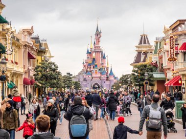 Paris, Fransa - 04 / 05 / 2022: Bulutlu havada Uyuyan Güzel Kalesi. İnsanlar Disneyland Parkları 'nın ünlü ve simgesel binasına yürüyorlar. Yolun iki tarafındaki komik dükkanlar..