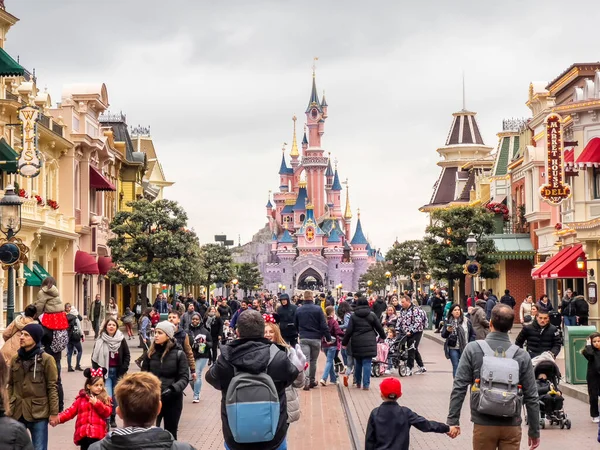 Paris, Fransa - 04 / 05 / 2022: Bulutlu havada Uyuyan Güzel Kalesi. İnsanlar Disneyland Parkları 'nın ünlü ve simgesel binasına yürüyorlar. Yolun iki tarafındaki komik dükkanlar..