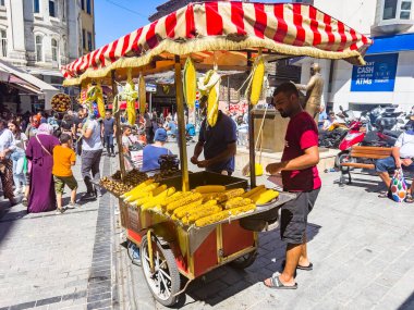Istanbul, Turkey, 07.14.2022: Man selling grilled corn. Street seller of fast food with boiled and grilled corn and chestnut on traditional Turkish cart at downtown district in summer