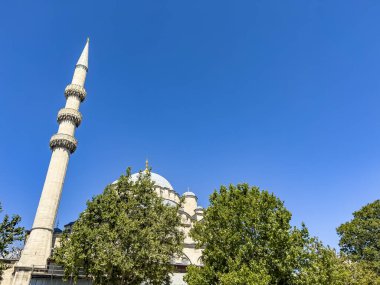 New Mosque (yeni Cami) partial view from below with minaret and green trees against blue sky background with copy space at Eminonu district in Istanbul, Turkey.