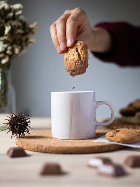 Breakfast with cookies and cocoa with milk, a hand dipping oatmeal cookies with chocolate chips into cacao - English breakfast close-up