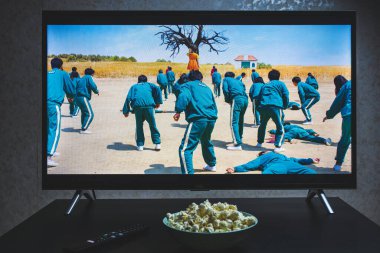Televizyonda Squid 'in yarışmasını izliyorum. Squid Game, Netflix 'te yayınlanan bir Güney Kore drama dizisidir.