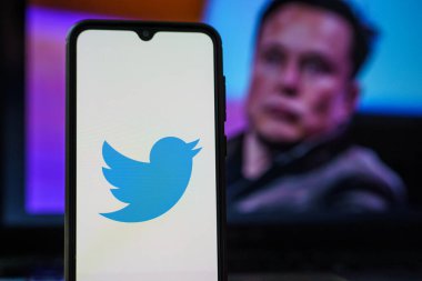 Twitter logosu akıllı telefonda ve Elon Musk arka planda. Elon Musk Twitter yönetim kuruluna katıldı
