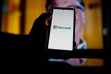 Ekranda Microsoft logosu ve arka planda Bill Gates. Microsoft 'un kurucularındandır.
