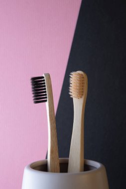 Pembe ve siyah arka planda seramik bir bardakta iki bambu diş fırçası. Bej ve siyah sakal. Ekoloji ve diş sağlığı kavramı.