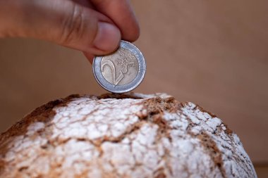 The hand puts the euro coin in the bread like in a money box. Economy, investment in food. food crisis. Agriculture. Agronomy. Bread production. Bakery. Business