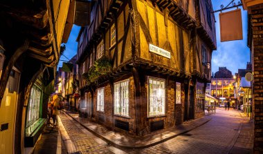A Chirstmas night view of Shambles, a historic street in York featuring preserved medieval timber-framed buildings with jettied floors, U clipart