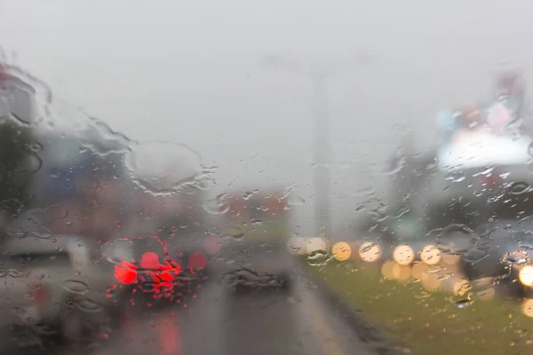 Blurry car silhouette seen through water drops on the car windshield.