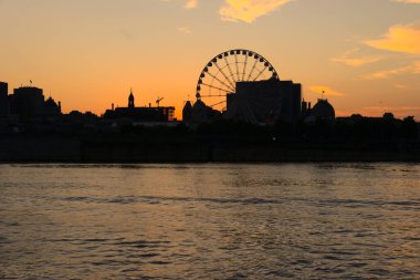Montreal Grand Ferris Wheel in Old Port at sunset. Reflections of sun rays on Saint Laurent river with a background of cloudy blue sky