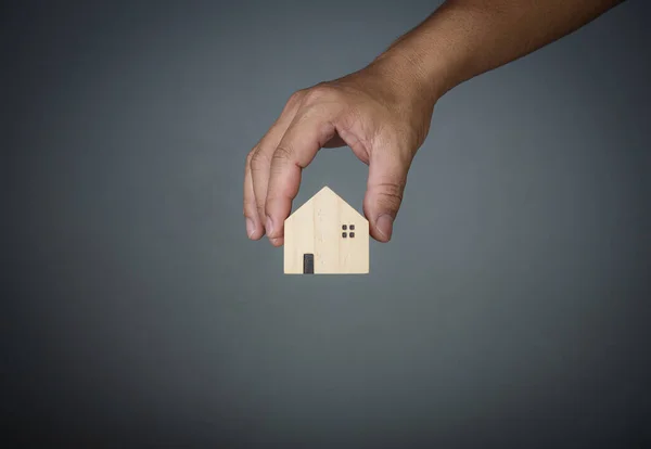 Ev satma kavramı. Bir el gri arka planda bir model evi tutuyor. Emlakçı ev, emlak sigortası ve güvenlik, uygun fiyatlı konut kavramları, ev sigortası komisyoncusu, satıcı.