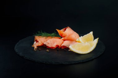 Smoked salmon with lemon Pepper and dill on black stone background.