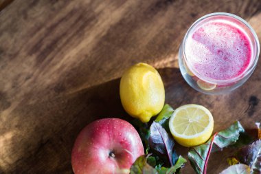 Top view of a glass of beetroot smoothie withapple,lemon and beetroot leaves on wooden background.