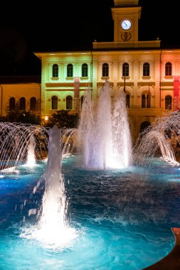 Cattolica, Italy - 04-08-2021: Illuminated and colored fountain with the Cattolica town hall in the background