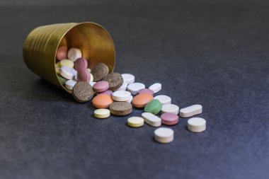 Pills spilling out of small brass glass. Different types of medicine on grey background.