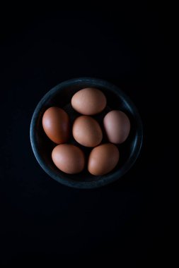 Taze kahverengi yumurtalar koyu arka plandaki kırsal kasede..