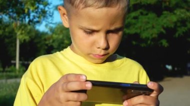 8 yaşında tatlı bir çocuk, yaz günü sokakta telefonuyla oyun oynuyormuş. Çocuklar ve aletler. Cep telefonuyla eğitim ve eğlence. Sosyal iletişim