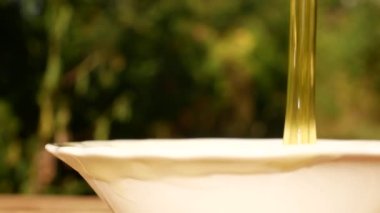 İnce bir bal akıntısı bir tabağa dökülür. Arka planda bir bahçe ve bir arı var. Bal toplayın. Organik ürün, bağışıklığı arttırmak için tatlı.