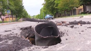 Bir mermi parçası asfalttaki bir kraterden görülebilir. Rus ordusu Ukrayna şehirlerini bombalıyor. Evin arka planında ve eski bir arabada.