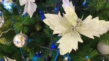 Noel ağacında Noel süslemeleri. Büyük parlak bir çiçek ve Noel ağacında beyaz parlak toplar. Arka planda Yeni Yıl çelengi ışıkları var.