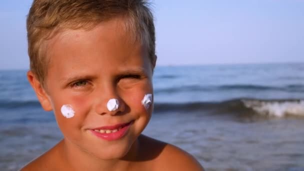 一个可爱的男孩 脸上带着防晒霜 背对着大海 日光浴时保护婴儿的皮肤 保护婴儿的皮肤免受阳光和晒伤 — 图库视频影像