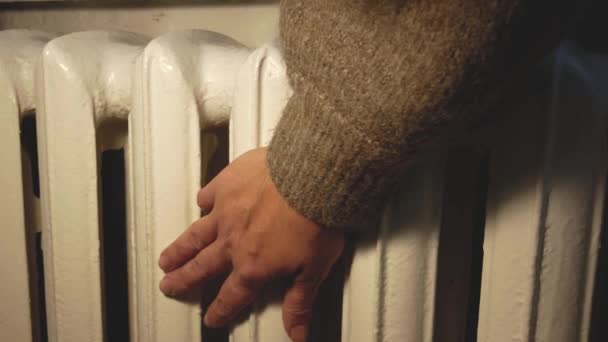一个穿着保暖毛衣的无法辨认的手碰到了一个旧电池 测试了电池的温度 冬天给房子加温 公寓里很冷 取暖价格的上涨 — 图库视频影像
