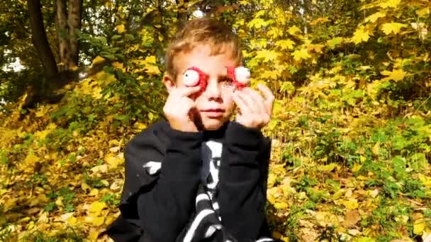 一个身穿黑色西服的男孩把可怕的目光投向自己 在万圣节期间让每个人都感到害怕 背景是一个秋天的公园 万圣快乐的节日 孩子们的聚会 — 图库视频影像