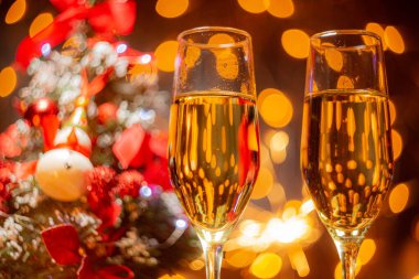 Noel ağacının arka planında şampanya bardakları ve yanan maytaplar. Noel ve Yeni Yıl kutlaması. Noel aydınlatması ve süslemesi