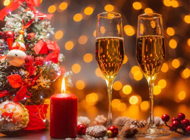 Noel ağacının arka planında şampanya bardakları ve yanan maytaplar. Noel ve Yeni Yıl kutlaması. Noel aydınlatması ve süslemesi