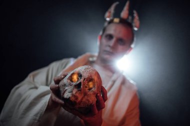 Ölü bir adamın makyajı ve kafasında bir taç olan bir adam. Duman ve ışığın özel efektleriyle kasvetli bir fotoğraf çekimi. Cadılar Bayramı için bir iblisi oynat. Karanlıktaki bir adamın silueti.