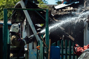 Bir itfaiyeci yanan bir eve su döker. Tahta bir binanın enkazı yangınla yok edildi. Kundaklamadan sonra kurtarma ekipleri kaza yerinde çalışıyor. Özel bir evin kalıntıları.